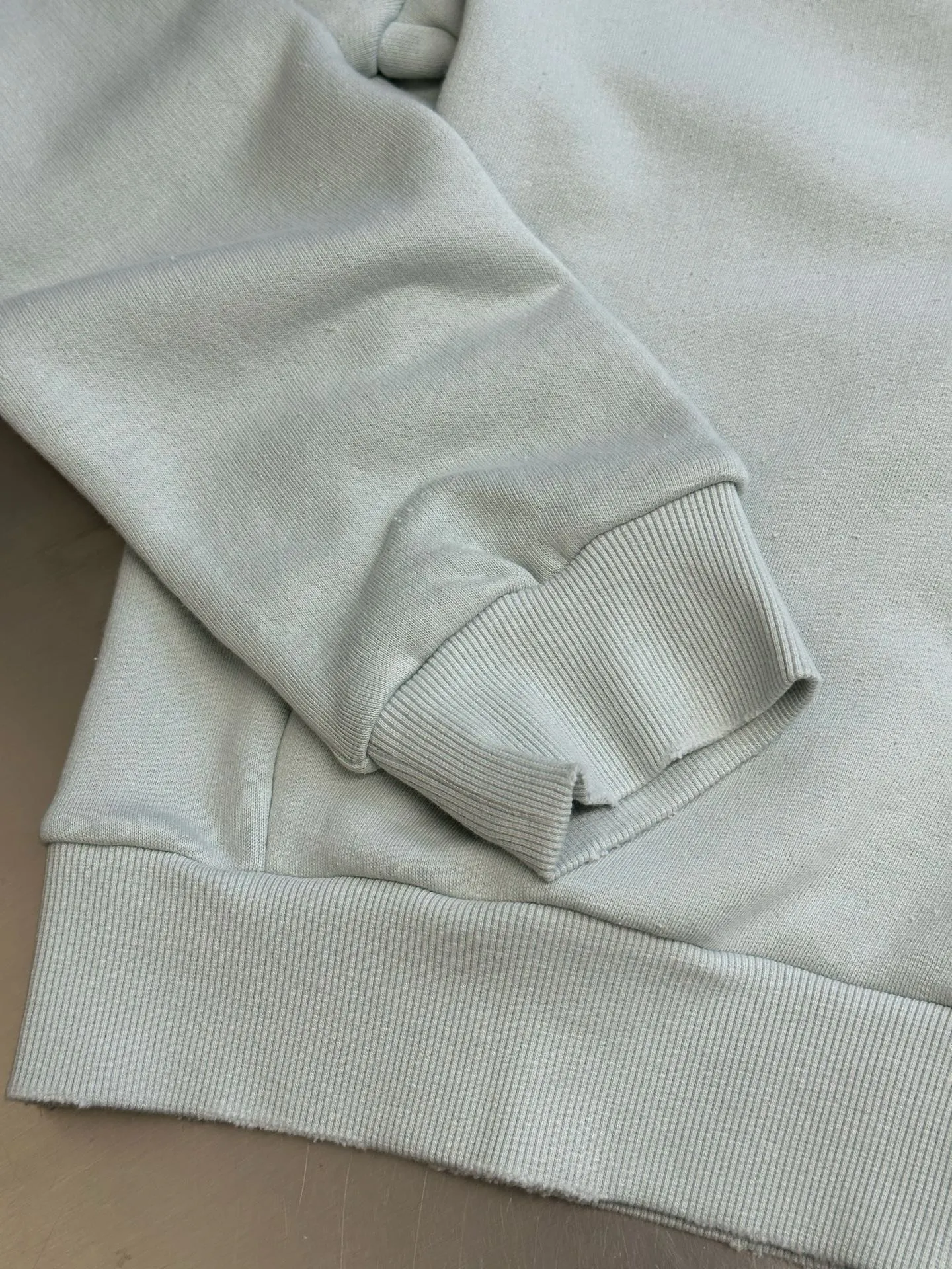Ac vintage collared zipper sweatshirt uses 32-count top layer and 40-count bottom layer of 3-strand composite fleece structure, with a weight of g/㎡. The 32-count yarn on the top layer is fine and smooth, giving the surface a smooth touch and excellent anti-pilling properties; the 40-count 3-ply yarn on the bottom layer is treated with a raising process to form a rich and soft fluff layer, providing excellent warmth and skin-friendly wrapping. With 21 2×2 ribs, the g/㎡ weight ensures that the collar, cuffs and hem have excellent tensile fatigue resistance and shape retention capabilities. During piece dyeing, the entire fabric is immersed in the dye vat after weaving, and the dye molecules fully penetrate into the fibers, ensuring full, deep colors and excellent color fastness. Each batch of dyeing produces subtle differences, making the color tone of the single product unique. On this basis, the paint is sprayed irregularly on the surface of the garment through manual spray painting to create a splash-like retro effect. The distressed processing of holes causes the color to fade and mottle in parts. The ribbed trim is also treated to form slight whitening and fluffing, which visually echoes the spray-painted effect on the body, making the new clothes appear as if they have been worn for a long time and exposed to the sun. The front logo stamp uses a slurry printing process. The printing slurry contains a special microcapsule foaming agent. After being baked at high temperature, the slurry layer expands to form three-dimensional bulges, and the surface presents a granular texture similar to inkjet paint. This process simulates the effect of random drops of pigment after being atomized during spray gun spraying. The edges of the pattern present a natural feathering transition, rather than the rigid boundaries of glue printing. The printing surface has a fine graininess and soft elasticity to the touch, forming a closed loop of the process with the distressed effect of the spray painting on the body. size：xs s m l